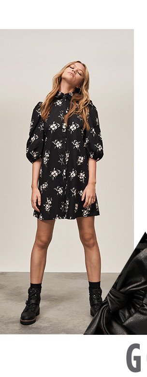 Woman with dark blonde hair poses with head back wearing black floral puff sleeve mini dress and black biker boots.