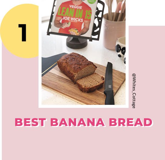 A fresh loaf of banana bread on a chopping board next to a bread knife, with a Joe Wicks cookbook in the background. 
