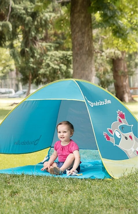 A young child sitting in a Badabulle anti-UV tent.