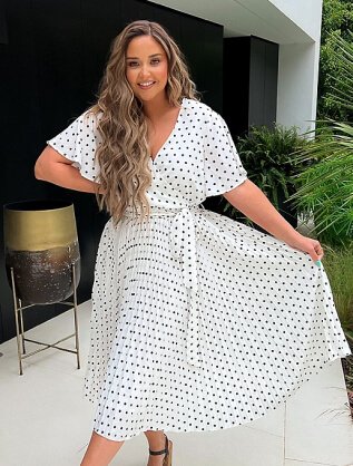 A woman posing in a black and white polka dot wrap dress.