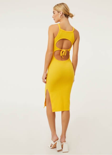 A woman posing in a yellow cutout dress and white heels.