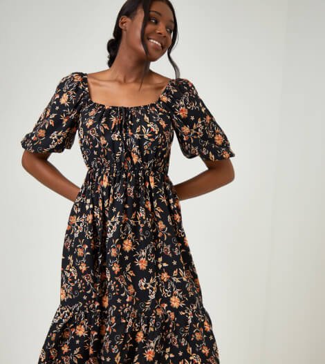 A smiling woman in a black floral floaty dress.