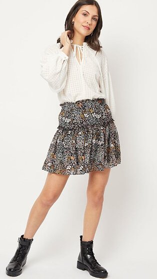 Woman wearing a dark floral print tiered mini skirt, white grid check blouse and black boots