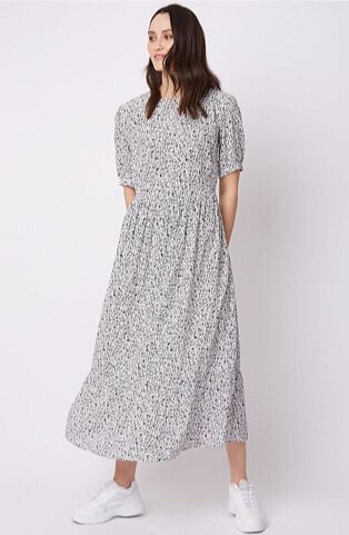 Woman wearing a black and white patterned tiered maxi dress with white trainers