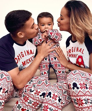 Woman and man lean into kiss cheek of baby while holding him in the air wearing matching navy and red Disney Mickey and Minnie family Christmas pyjama set.