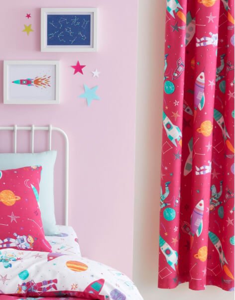 A pale pink bedroom with bright pink space themed curtains, bedding and decor items.