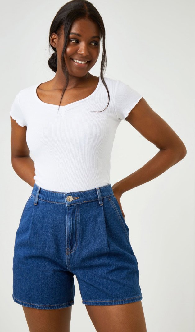 A smiling woman wearing denim shorts and a white t-shirt.