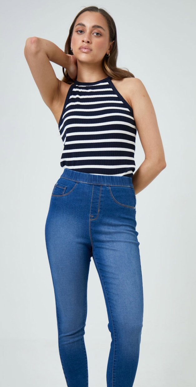 A woman posing in denim jeggings, a navy and white striped racer vest and black sandals.