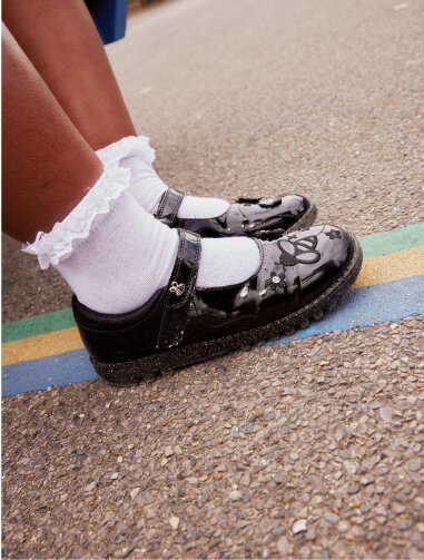 A close shot of a child wearing white frilly socks and black bee patent school shoes.