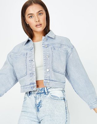 Woman poses wearing grey cropped t-shirt, light wash cropped denim jacket and acid wash blue jeans.