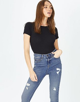 Woman poses with hand in pocket wearing black t-shirt and blue distressed skinny jeans.