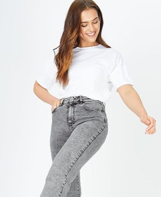 Woman smiles with one hand in pocket wearing grey acid wash mom jeans and white t-shirt.