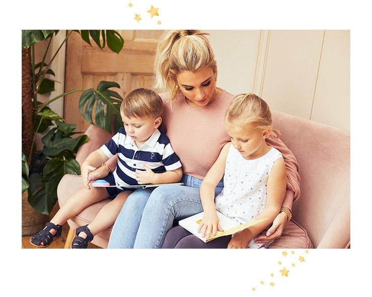 Billie Faiers on a pink sofa wearing a pink jumper and jeans with her son and daughter reading books, both in Billie Faiers clothing