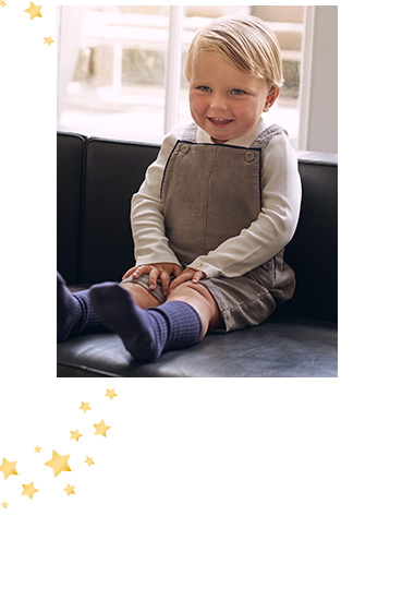 Child sitting down wearing brown dungarees and white long sleeve top