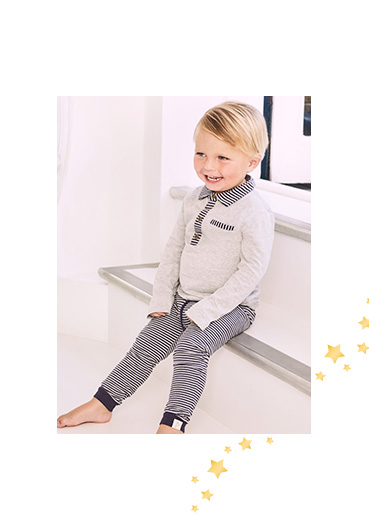 Child sitting down wearing a grey long sleeve top and striped navy and grey bottoms