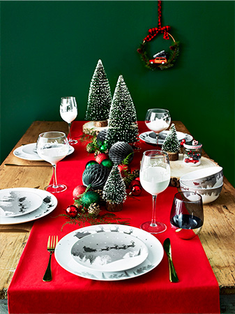 Table with red tablecloth, festive crockery, gold cutlery and red and green ornaments