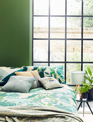 Gif of bed with leaf print bedding and matching cushions, and a kitchen table surrounded by green plants