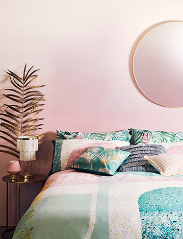 Pink palm leaf print bedding with matching pillows and cushions, and a white dinner table with pastel dinnerware