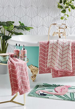 Decorated bathroom with green bathtub with pink towels rapped over the sides and a flamingo bath matt