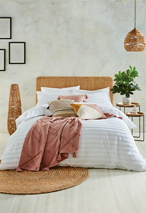 Double bed in white bedsheets with soft pink blanket and pillows over the top