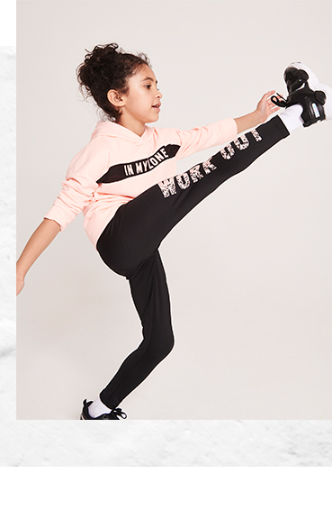 Girl wearing pink sports hoodie and black bottoms performing a high kick
