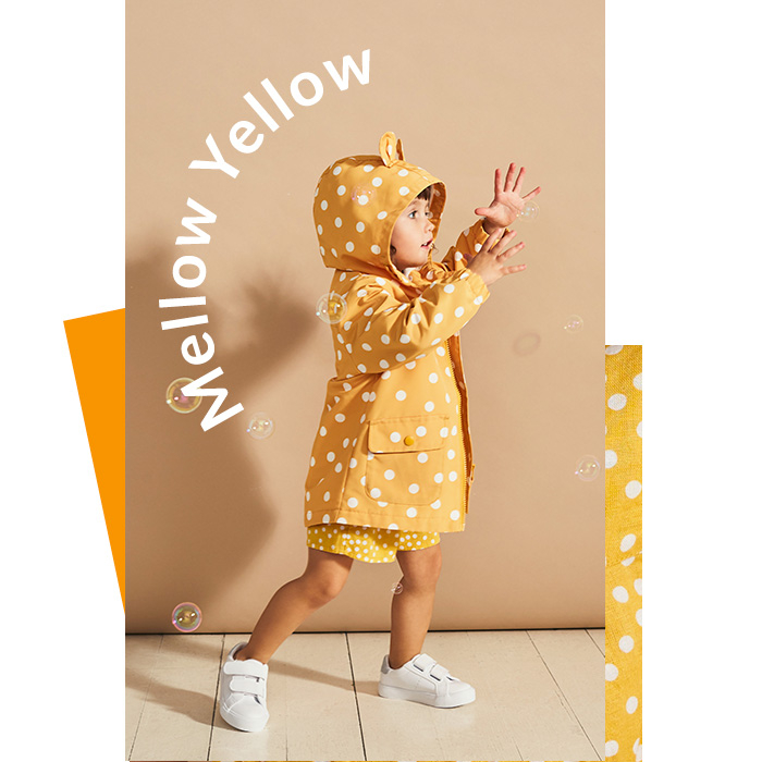 Girl catching bubbles wearing mustard yellow polka dot raincoat with bear ears, matching skirt and white trainers