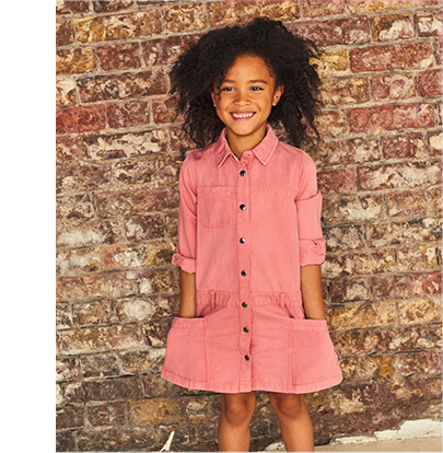 Girl smiling with her hands in her pocket wearing a pink shirt dress