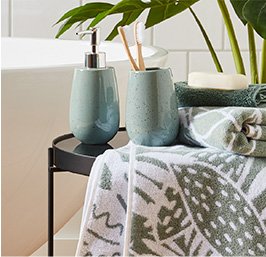 A side table with a dispenser and tumbler and leaf print towels