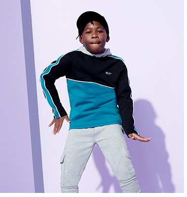 A dancing boy wearing a blue and black jumper with grey joggers.