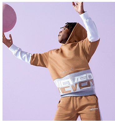 A boy playing with a ball wearing a tan slogan hoodie and joggers set.
