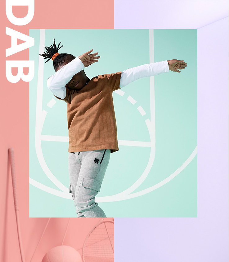 A boy dabbing wearing a tan and white long sleeve top with grey joggers.