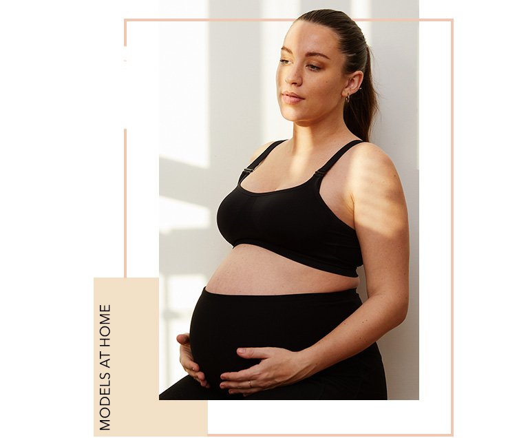 Woman with long dark ponytail poses wearing black maternity bra and bump band.