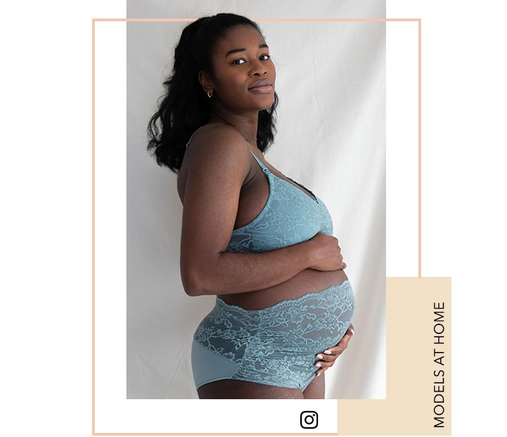 Woman with long black hair poses side on wearing maternity teal lace lingerie in front of a white curtain.