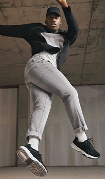Man in a dance pose wearing a sweatshirt, grey jeans, a cap and black trainers