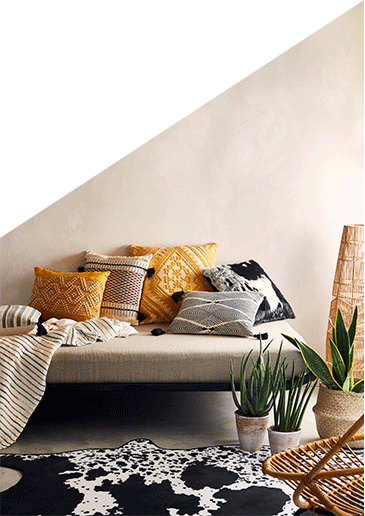 Sofa with an assortment of cushions, a striped throw, a cow print rug and artificial plants in pots