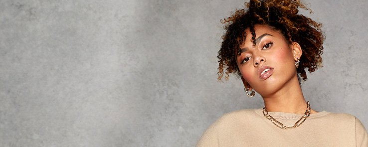 Close up of Phoenix Brown tilting head wearing beige co-ord knit crop top and gold-tone necklace.