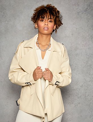 Phoenix Brown poses wearing cream collared rib knit dress and light beige cropped trench jacket.