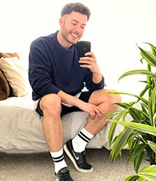 Man wearing a navy jumper and shorts taking a selfie