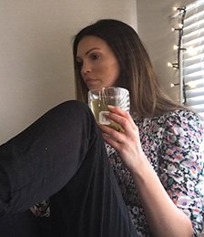 Woman holding a drinking glass wearing a pattered blouse and black jeans