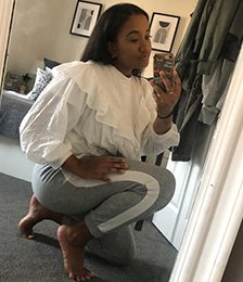 Woman taking a selfie wearing a white blouse and grey joggers