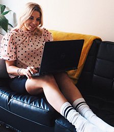 Woman wearing a pink polka dot blouse on her laptop on the sofa