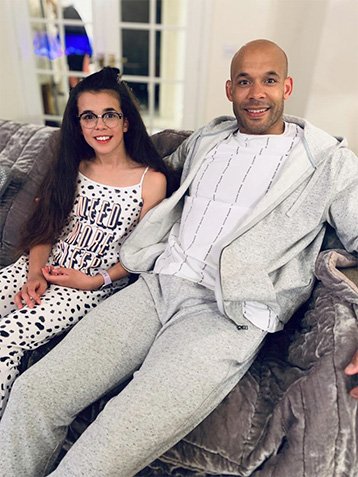 Girl and man sat on a sofa in grey joggers and hoody