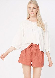 Woman wearing terracotta pink textured shorts with a white long sleeve blouse