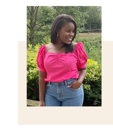 Woman outside wearing a pink poplin sweetheart neck shirred blouse with jeans