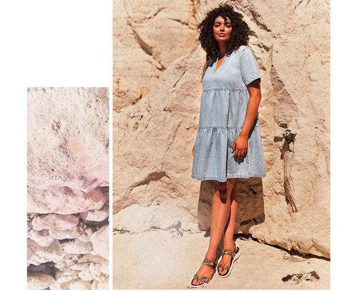 Woman in front of a large rock wall wearing a light wash denim v-neck tired smock dress with strappy sandals