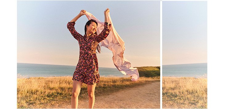 Woman on a beach path wearing a floral print ruffle hem tea dress and holding flowing fabric