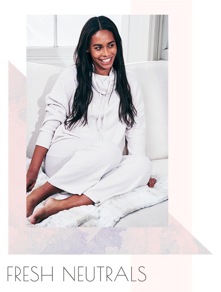 A woman sitting on a sofa wearing a cream cowl neck jumper with matching straight fit lounge joggers