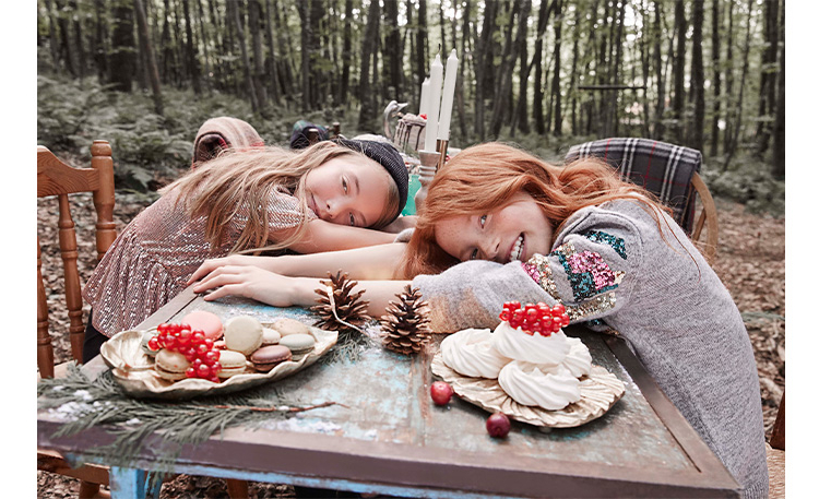 Two girls sitting down with their head and arms on a wooden table 