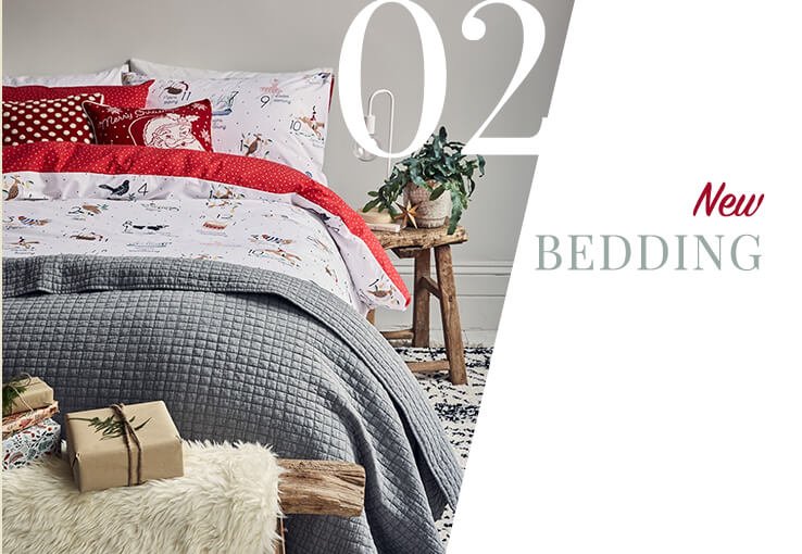 Double bed with wooden side table, white lamp and plant with 12 days of Christmas reversible duvet set, check print throw and wrapped presents at the bottom of the bed.