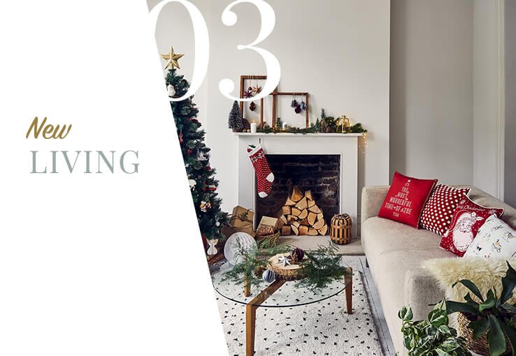 Cream sofa with assortment of red and white Christmas scatter cushions and cream faux fur throw next to fireplace with hanging stocking and festive decorations.